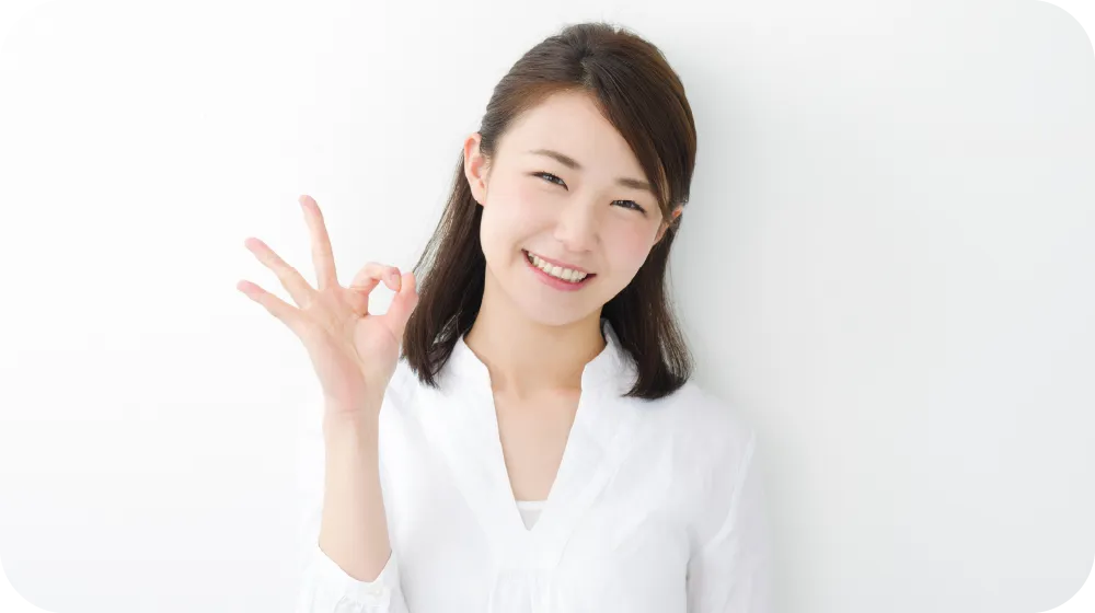 白い服を着た女性が笑顔でOKサインを出している様子。